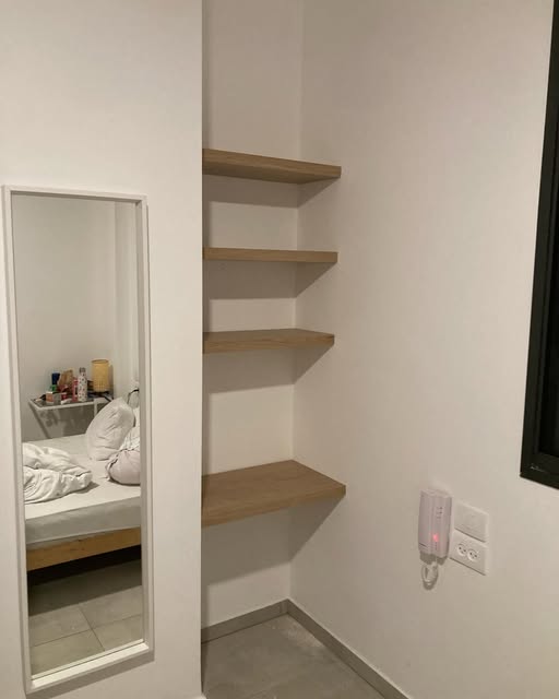 Wall mirror beside four floating wood shelves.